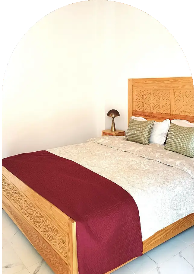 Moroccan carved wooden bed with neatly arranged linens in a riad bedroom in Essaouira