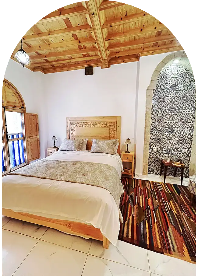 Moroccan carved wooden bed with neatly arranged linens in a riad bedroom in Essaouira